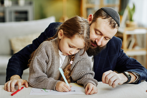 Portrait of caring jewish father drawing pictures with daughter at home