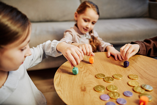 Portrait of three children playing traditional dreidel game in cozy warm lighting, copy space