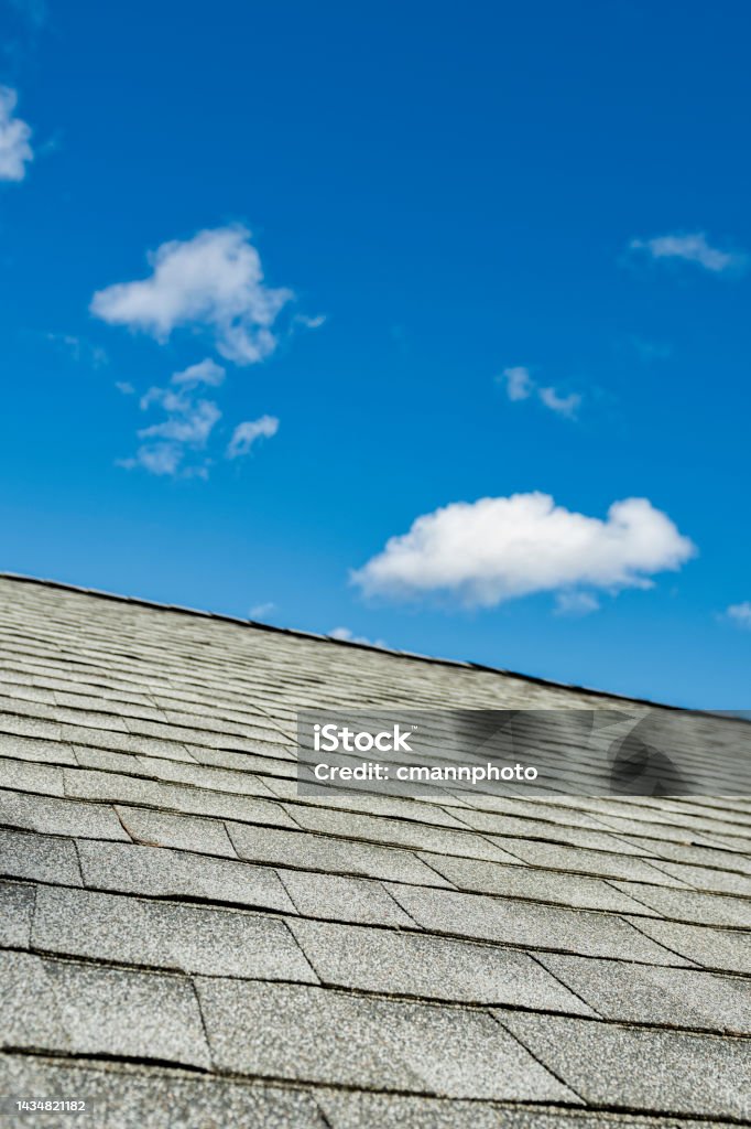 Newly installed architectural shingles on a residential home sky in background Newly installed gray architectural asphalt shingles on a residential house during a remodeling project, with blue sky and puffy clouds in background. Architectural Feature Stock Photo