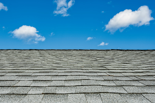 Newly installed gray architectural asphalt shingles on a residential house during a remodeling project, with blue sky and puffy clouds in background.