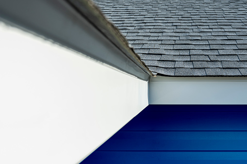 A close-up of newly installed gray architectural shingles, aluminum fascia and perforated soffit on a residential house with blue siding during a remodeling project.