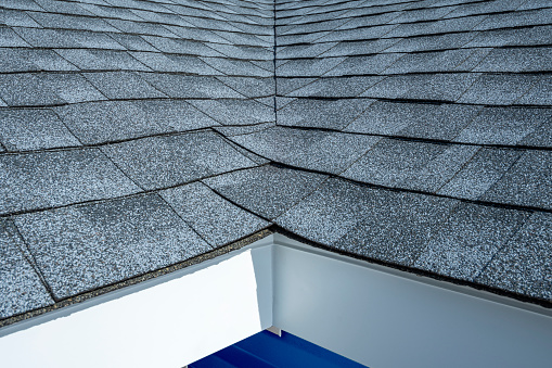 A close-up of newly installed gray architectural shingles, aluminum fascia and perforated soffit on a residential house with blue siding during a remodeling project.