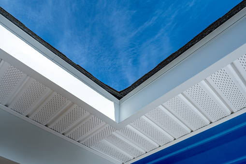 Looking up at newly installed aluminum fascia, perforated soffit and shingles on a residential house with blue siding during a remodeling project.