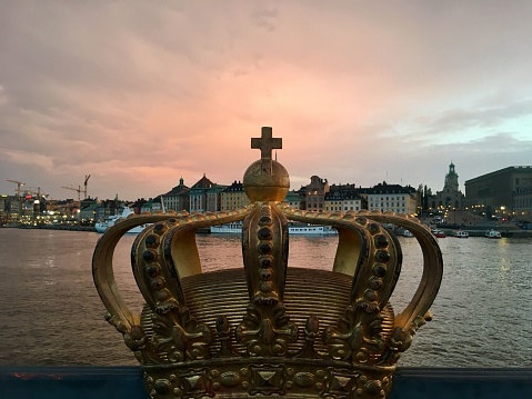 A closeup shot of the Gilded Crown on Skeppsholmsbron with Stockholm city in the background against the sunset sky