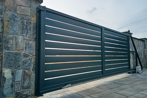 Wide automatic sliding gate with remote control installed in high stone fense wall. Security and protection concept.