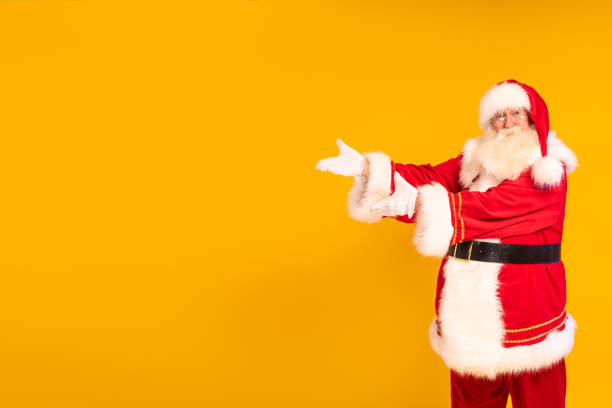 istock Santa Claus showing empty advertisement place on yellow studio background with copy space. Christmas is coming. Time for xmas gifts. 1434825795