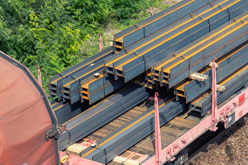 Heap pile heavy raw rusted steel iron beam girders loaded on railroad cargo freight carriage. Metal goods factory plant products shipping and logistics. Metallurgy industrial transportation service.