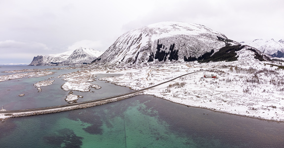 Aerial snowy winter view of Grimsoystraumen bridge and the E10 main road approaching it in the Lofoten Islands of Northern Norway