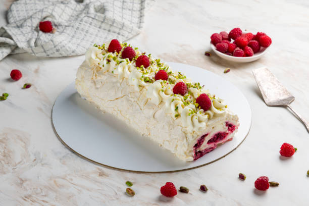 meringue roll with raspberries and pistachios on white marble table