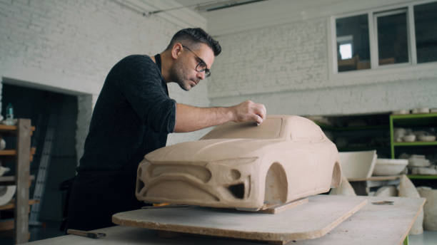 陶芸家は粘土で作られた未完成の車の彫刻のデザインの詳細に取り組んでいます - industrial designer ストックフォトと画像