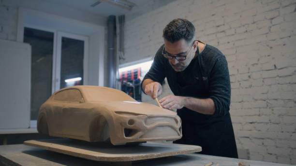Experienced designer works on the sculpture of the car using wooden shaping tool Experienced designer works on the sculpture of the car made of raw clay using wooden shaping tool to smooth out the surface. Hand made car sculpture made of clay. Automotive industry. industrial designer stock pictures, royalty-free photos & images