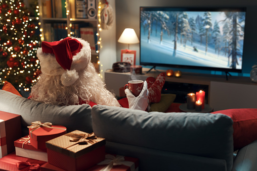 Happy Santa Claus relaxing on the couch at home and watching movies on TV