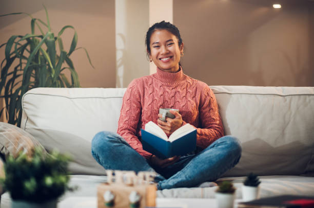 istock Asian woman siting on the couch at home while reading a book and drinking coffee 1434849194