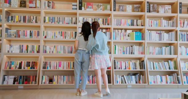 asian girl friends finding book in front of bookshelf at the bookstore