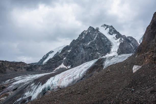 istock Dramatic landscape with hanging glacier against large snow mountain with sharp rocky pinnacle under gray cloudy sky. Glacier with icy cornice in high altitude. Gloomy scenery in mountains in overcast. 1434866364