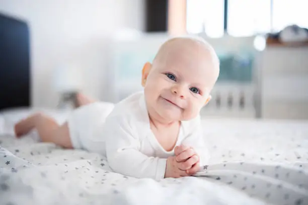 Joyful little baby boy smiling and laying on front on bed.