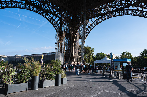 Paris, France - August 27 2022: People queueing to go up the Eiffel tower. Iron structure building, distinctive symbol and famous tourist attraction of Paris, France, selective focus