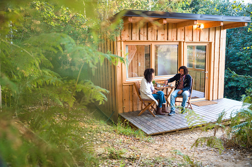 Full length shot of Hispanic couple having coffee on a patio of their glamping cabin.