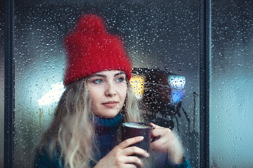 Music of rain. Side shot of serene latin woman relax by window with closed eyes listen sound of raindrops feel pleasure. Calm young lady enjoy breathing fresh ozonized air after rainstorm. Copy space.