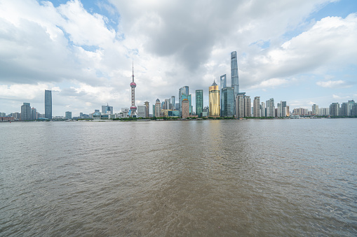 shanghai skyline in cloudy day, showing the Huangpu river with passing cargo ships, financial district and cloudy sky background