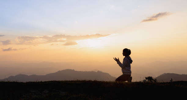 silueta de una mujer rezando afuera en un hermoso paisaje en la cima de la montaña, copia espacio del hombre levantar la mano en la cima de la montaña y el cielo del atardecer fondo abstracto. - praying fotografías e imágenes de stock