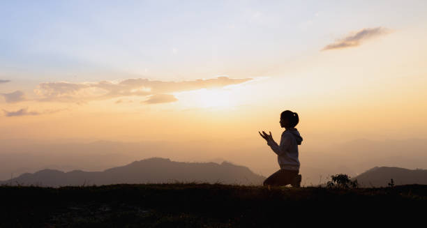Silhouette of a woman praying outside at beautiful landscape at the top of the mountain, Copy space of man rise hand up on top of mountain and sunset sky abstract background. Silhouette of a woman praying outside at beautiful landscape at the top of the mountain, Copy space of man rise hand up on top of mountain and sunset sky abstract background. prayer position stock pictures, royalty-free photos & images