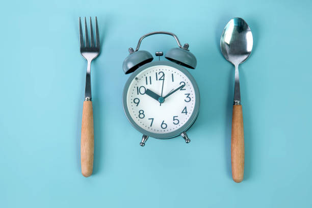 istock Time to lose weight, intermittent fasting eating control or time to diet concept, alarm clock and a spoon decoration on a blue background 1434887878