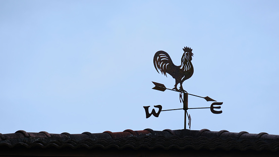 The old wind vane with a rooster symbol icon on the roof, traditional technology equipment for forecast and measuring windy weather in the air, vintage decoration, aiming wind direction instrument.