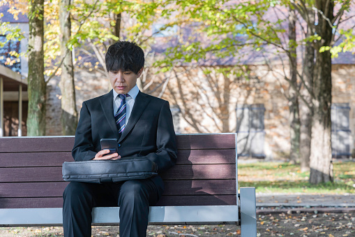 Senior businessman sits pensively on the bench in the park during the work break.