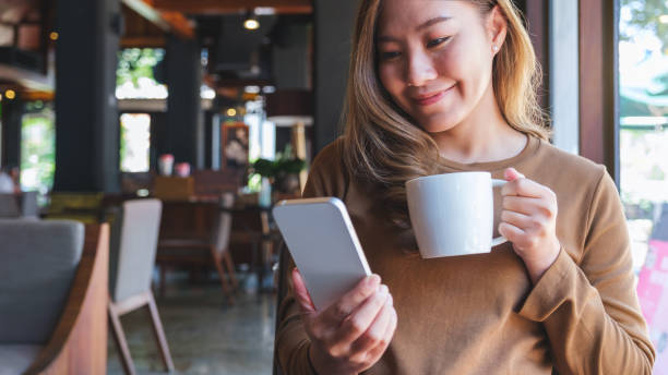 istock Portrait image of a young woman holding and using mobile phone while drinking coffee in cafe 1434893819