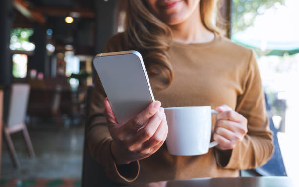 istock Closeup image of a young woman holding and using mobile phone while drinking coffee in cafe 1434893823