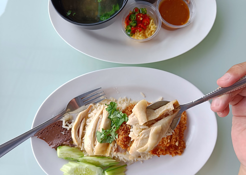 Boiled chicken rice on a spoon served with soup and dipping sauce, top view. The most popular street food in Thailand is called Khao Mun Gai.