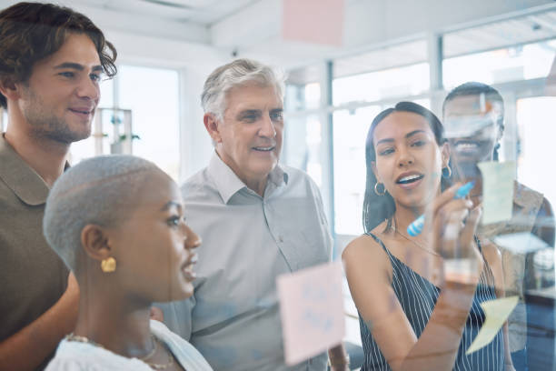istock Business people planning with sticky note in meeting, team collaboration during presentation on glass in office and teaching analytics to employee in workshop. Manager training workers on strategy 1434900516