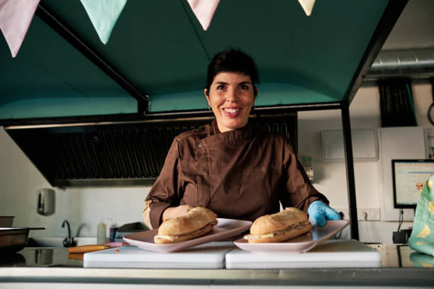 istock Woman looking at camera and smiling while serving two sandwiches at restaurant counter. 1434902744