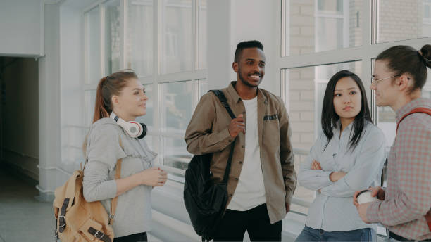 istock Young beautiful caucasian female student is standing in front of her three multi-ethnic groupmates discussing something together in positive way near window 1434906635