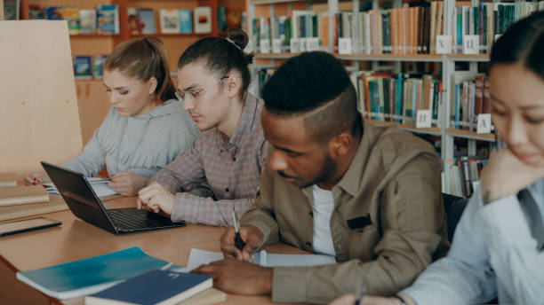 istock Focus on hipster male student in glasses using laptop computer while preparing for exams in university library with his classmates 1434908553