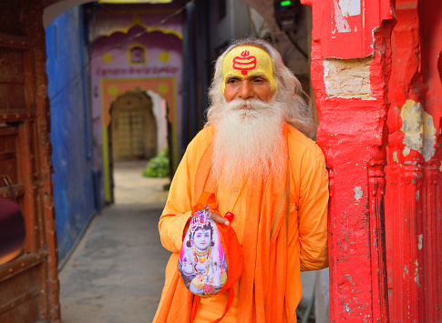 Pushkar, India - November 01, 2017: A hindu priest dressed in saffron clothes standing in front of a temple.