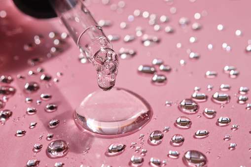 Pipette, drop and splashes of micellar water on a pink background.