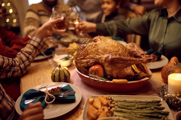 Close up of stuffed turkey during Thanksgiving meal with family toasting in the background. Close up of Thanksgiving turkey during family dinner at dining table. main course stock pictures, royalty-free photos & images