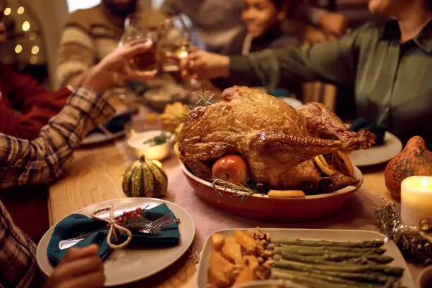 Photo of Close up of stuffed turkey during Thanksgiving meal with family toasting in the background.