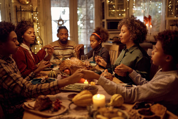 afro-americana família estendida dizendo graça enquanto tem refeição de ação de graças na mesa de jantar. - family thanksgiving dinner praying - fotografias e filmes do acervo