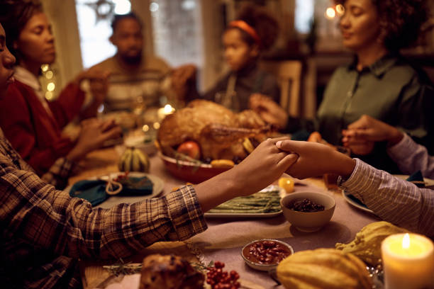 nahaufnahme von schwarzen brüdern, die händchen halten, während sie mit ihrer familie während des abendessens an thanksgiving beten. - thanksgiving stock-fotos und bilder