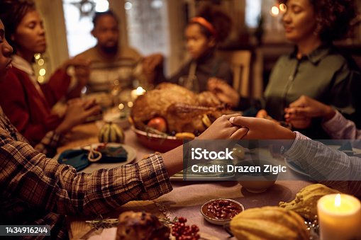 istock Close up of black brothers holding hands while praying with their family during dinner on Thanksgiving. 1434916244