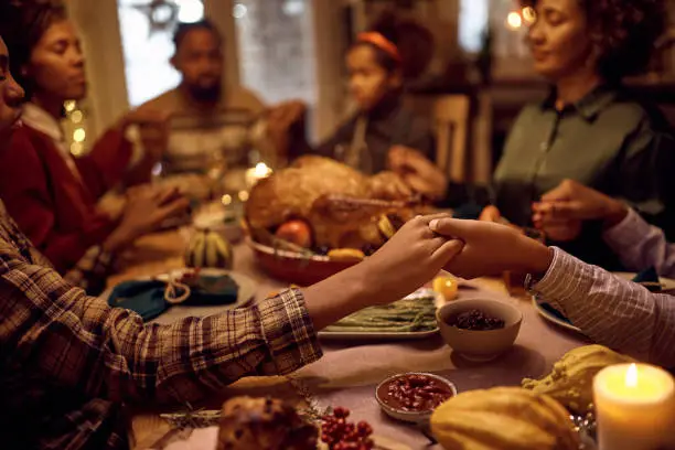 Photo of Close up of black brothers holding hands while praying with their family during dinner on Thanksgiving.