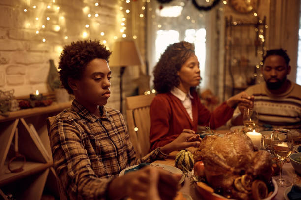 黒人の少年と彼の家族は、感謝祭のダイニングテーブルで夕食を食べながら優雅さを語っています。 - praying saying grace dinner meal ストックフォトと画像