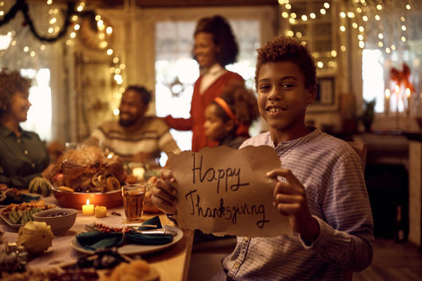 istock Smiling black boy with Happy Thanksgiving message during family dinner at dining table. 1434916274