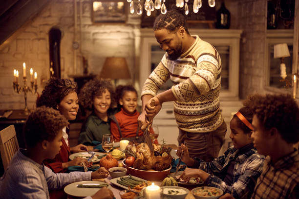 szczęśliwy czarny mężczyzna rzeźbi indyka na święto dziękczynienia podczas rodzinnego posiłku przy stole. - roast turkey turkey cutting roasted zdjęcia i obrazy z banku zdjęć