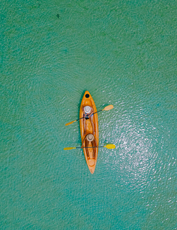 Men and women in a Kayak peddling in the turquoise-colored ocean of the tropical Island of Koh Mak Thailand. men and women in kayaks at a blue ocean and white beach with palm trees