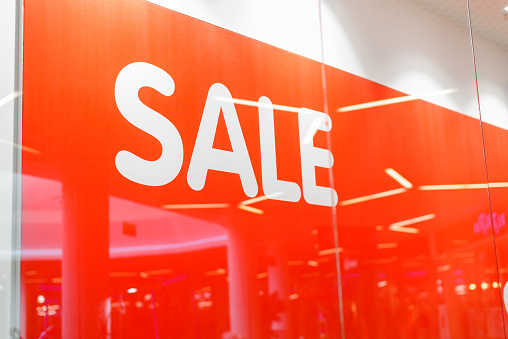 The inscription in large letters SALE on a red background on a shop window. Discount announcement banner, holiday sale, black friday concept.