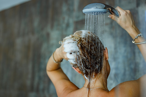 Back view of a woman washing her hair with a shampoo in bathroom. Copy space.